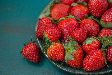 Ripe strawberries in a plate close-up on a blue-green background