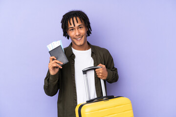 Young african american man isolated on purple background in vacation with suitcase and passport