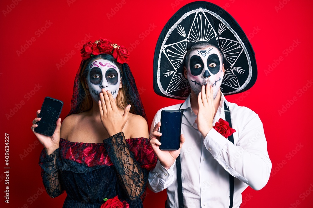 Sticker couple wearing day of the dead costume holding smartphone showing screen covering mouth with hand, s