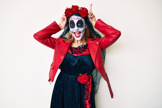 Woman wearing day of the dead costume over white posing funny and crazy with fingers on head as bunny ears, smiling cheerful