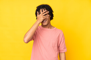 Young african american man isolated on yellow background covering eyes by hands and smiling