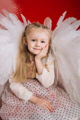 little girl 4 years old in white angel wings on a red latex background in the studio for valentine's day