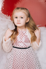 little girl 4 years old in white angel wings on a red latex background in the studio for valentine's day