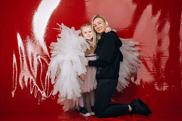 little girl 4 years old in white angel wings on a red latex background in the studio for valentine's day