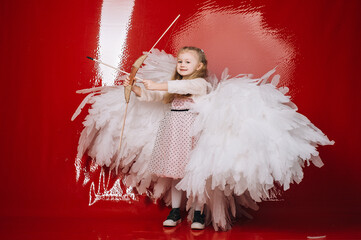 little girl 4 years old in white angel wings on a red latex background in the studio for valentine's day