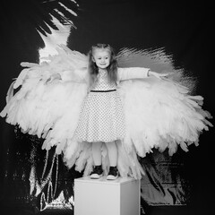 little girl 4 years old in white angel wings on a red latex background in the studio for valentine's day