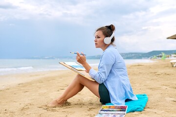 Mature woman sitting on sandy beach drawing sketch of sea