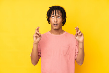 Young african american man isolated on yellow background with fingers crossing and wishing the best