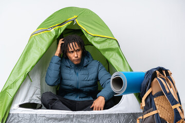 Young african american man inside a camping green tent having doubts while scratching head