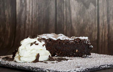 Piece of homemade moist chocolate cake with whipped cream against a wooden background
