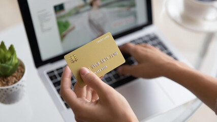 Close up young woman holding plastic bank card in hands, enjoying shopping online on laptop, female...
