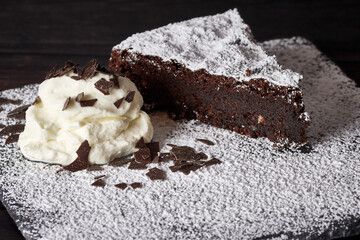 Slice of homemade chocolate cake with whipped cream, sprinkles and powdered sugar on a square plate