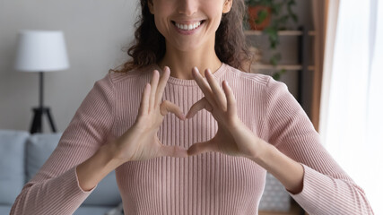 Close up cropped image smiling young woman showing heart love sign with fingers, feeling grateful...