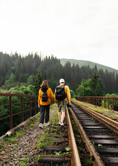 Fototapeta na wymiar couple of young people walking holding hands on the railway track on a viaduct in the mountains on a background of beautiful landscape. Vertical