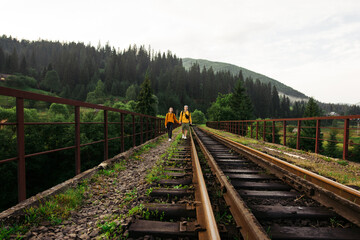 Beautiful couple of young people walking holding hands on the railway track on a viaduct in the mountains on a background of beautiful landscape.