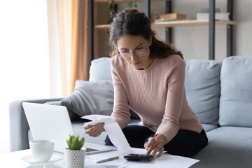 Focused smart millennial woman in eyeglasses busy with financial paperwork, calculating utility...