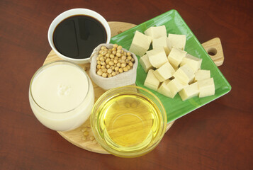 Soybeans and assortment of soy products - milk, sauce, oil and tofu on cutting board.