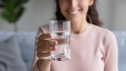 Close up focus on glass with mineral clean water in female hands. Happy sincere young woman showing...