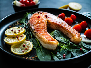 Fried salmon steak with spinach, lemon and cherry tomatoes  served on black plate on wooden table
