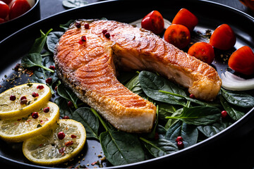 Fried salmon steak with spinach, lemon and cherry tomatoes  served on black plate on wooden table
