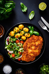 Breaded fried pork chop, French fries and vegetables on white background
