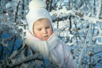 A child in a warm white hat and scarf plays with snow while walking in the winter forest, snowfall, winter magic, bright emotion, protecting the skin from frost