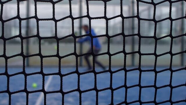 Slowmotion through grid view of paddle tennis man playing on blue court outdoors. One caucasian padle player sportman hitting the ball. Racquet sport game Concept.-Dan