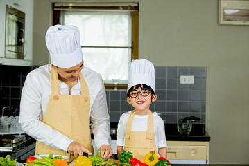 Cute asian little boy with  father  in uniform chef preparing cooking fresh salad in kitchen at home