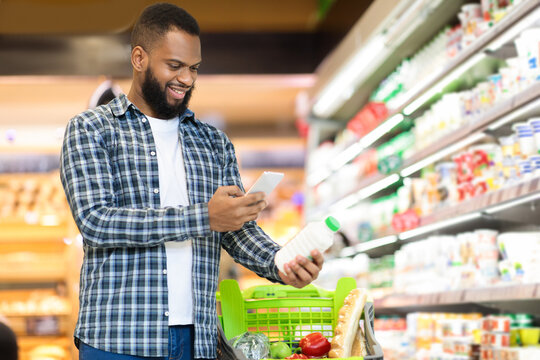 Guy Scanning Product Via Phone Doing Grocery Shopping In Supermarket