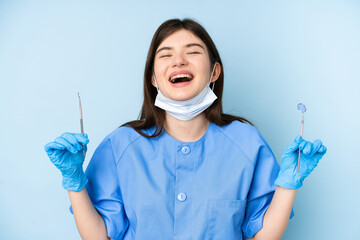 Young dentist woman holding tools over isolated blue background