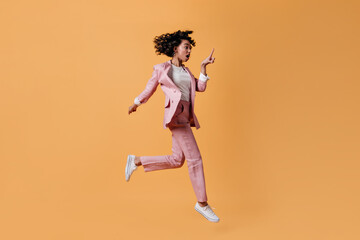Fototapeta na wymiar Shocked female model jumping on yellow background. Full length view of emotional mixed race woman in pink attire.