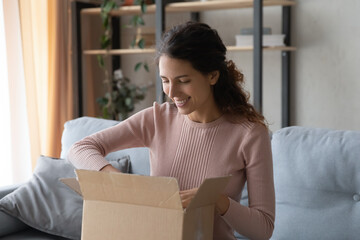 Smiling attractive woman opening big carton box, feeling curious of unpacking internet store order at home. Happy millennial female client satisfied with fast delivery service, online shopping concept
