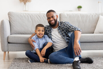 African Father And Son Embracing Sitting On Floor At Home