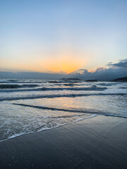 Orange sunrays shining from the clouds at the evening sea, sand beach, clear sky