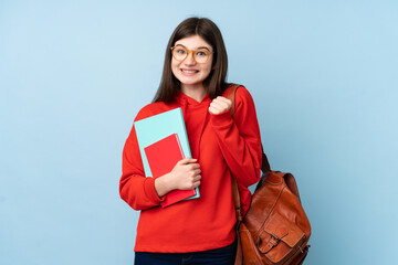Young Ukrainian teenager student girl holding a salad over isolated blue background celebrating a...