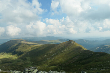 Fototapeta premium A panoramic view on the distant Grosse Speikkogel in Austrian Alps. The mountains around are lush green. A bit of overcast, blue sky. Soft and edgeless mountains. Achievement and completion.