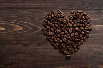 Still life of roasted coffee grains in the shape of a heart and love symbol on a brown wooden background