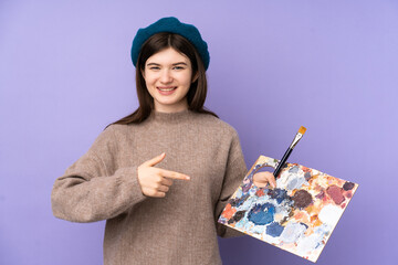 Ukrainian Young artist girl holding a palette over isolated purple background and pointing it