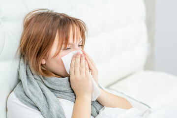Diseased girl sitting on the bed and blowing her nose in tissue