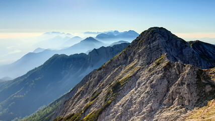 Panoramic view on the haze shrouded valley from the way to Mittagskogel in Austrian Alps. Clear and sunny day. Endless mountain chains. Outdoor activity. Barren top of the mountains, lush lower parts