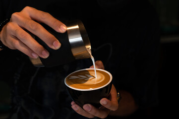 Pouring latte art into the black coffee cup