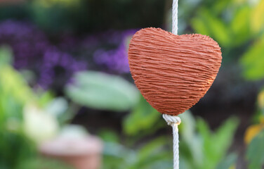 Closeup of brown heart-shape handmade earthenware hanging by white rope with natural background. 