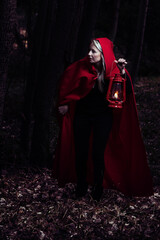 Attractive woman dressed a little red riding-hood walk in a dark forest with lantern - 409647873