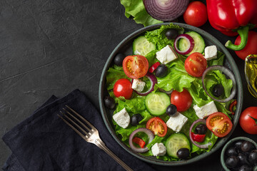 Greek salad. Vegetable salad from fresh vegetables, feta cheese and olives in a plate over towel with fork on black table