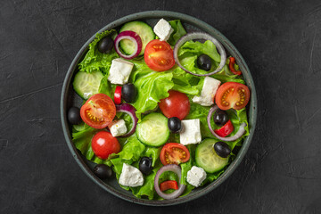 Greek salad with fresh vegetables, feta cheese and olives in a plate on black background. Top view. Vegetarian food