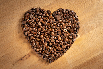 Brown freshly roasted coffee beans shaped into a love heart on oak wood background