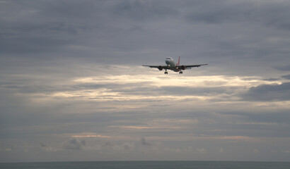 Naklejka na ściany i meble Closeup of an airplane flying over the sea in twilight evening of rainy day. 