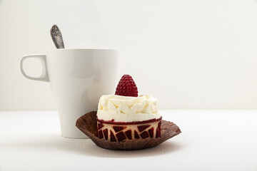 Tea in a white mug and spoon, with a raspberry cake on a light background