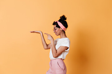 Side view of pretty brunette girl gesturing on yellow background. Studio shot of charming young woman with pink ribbon.
