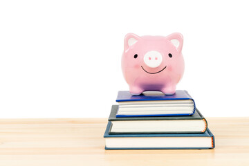 Pink piggy bank on top of books on wooden desk on white background, concept saving for education...